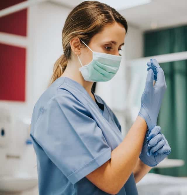 Female medical professional with mask on, putting on gloves