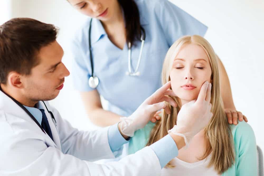 Consultation for aesthetics procedure, medical professionals assess woman's face.