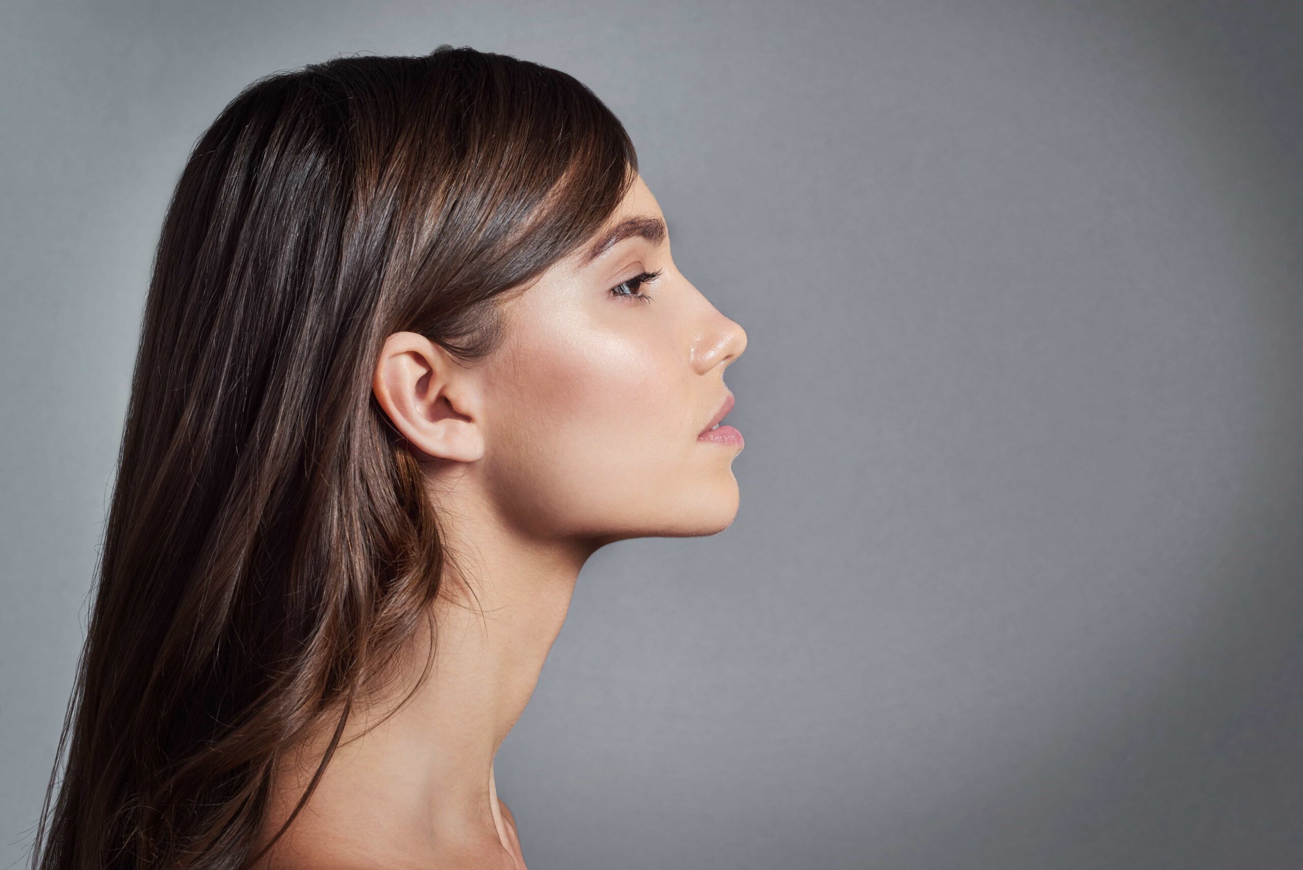 Profile view of a young woman with long dark hair, highlighting the clean lines of her straight nose, defined jawline, and neck contour.
