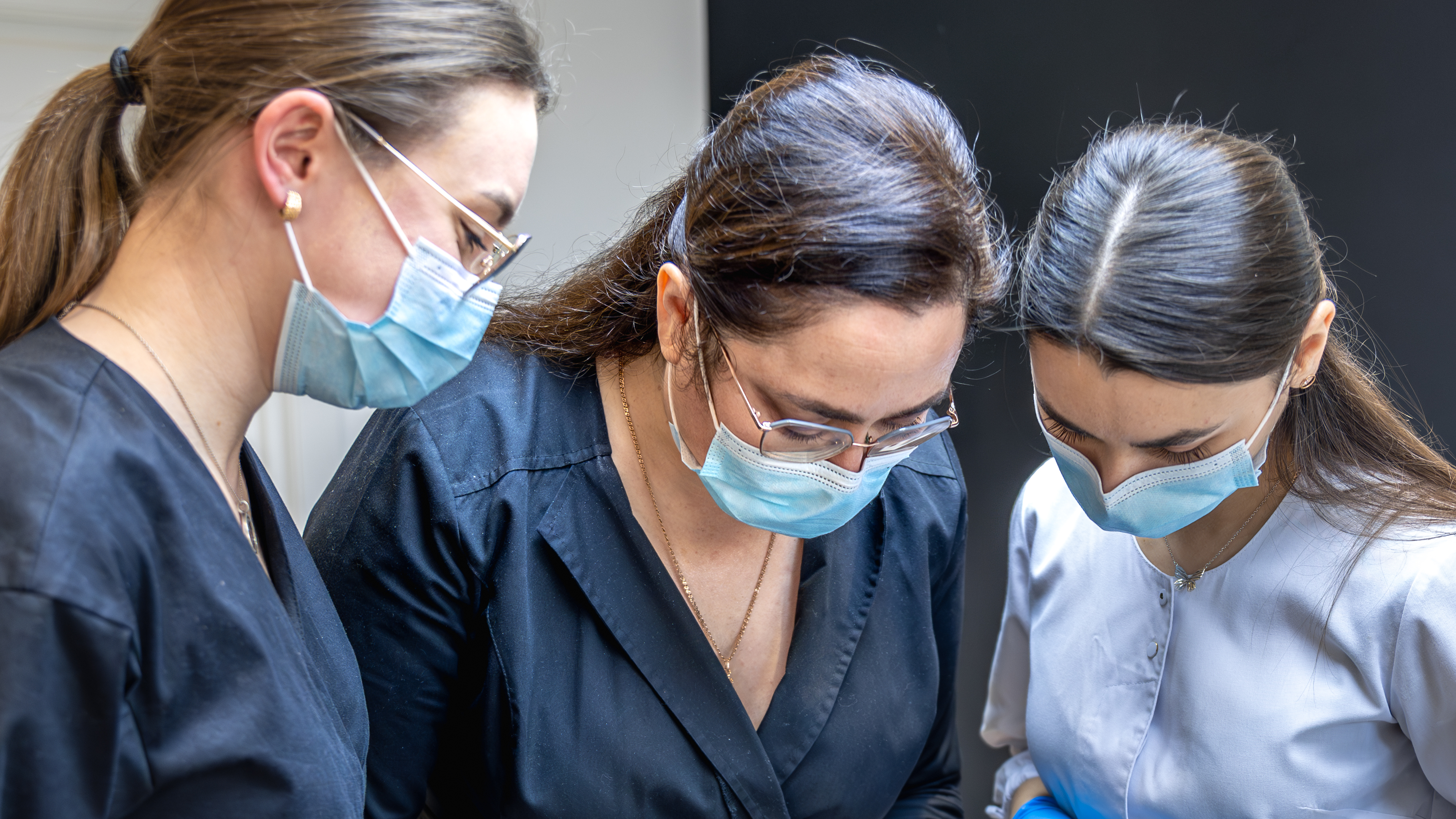 Three nurses examining a patient, with one teaching two apprentices, in a clinical setting. Relevant for Medical Malpractice Insurance.